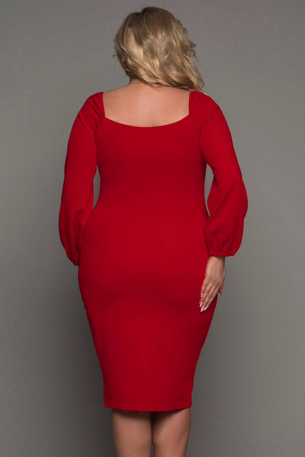 A woman wearing a blue long sleeve dress with a front knot detail at the waist, in a plus size midi length