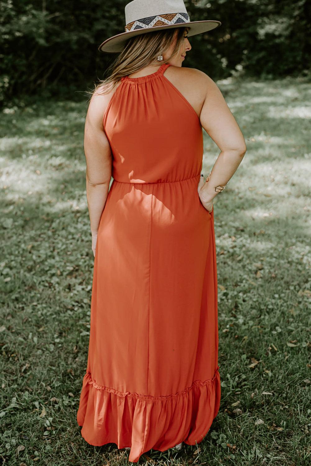 Plus size fashionista stunningly showcasing a sleeveless long dress featuring an elegant ruffled hem, perfect for summertime outings and special celebrations.