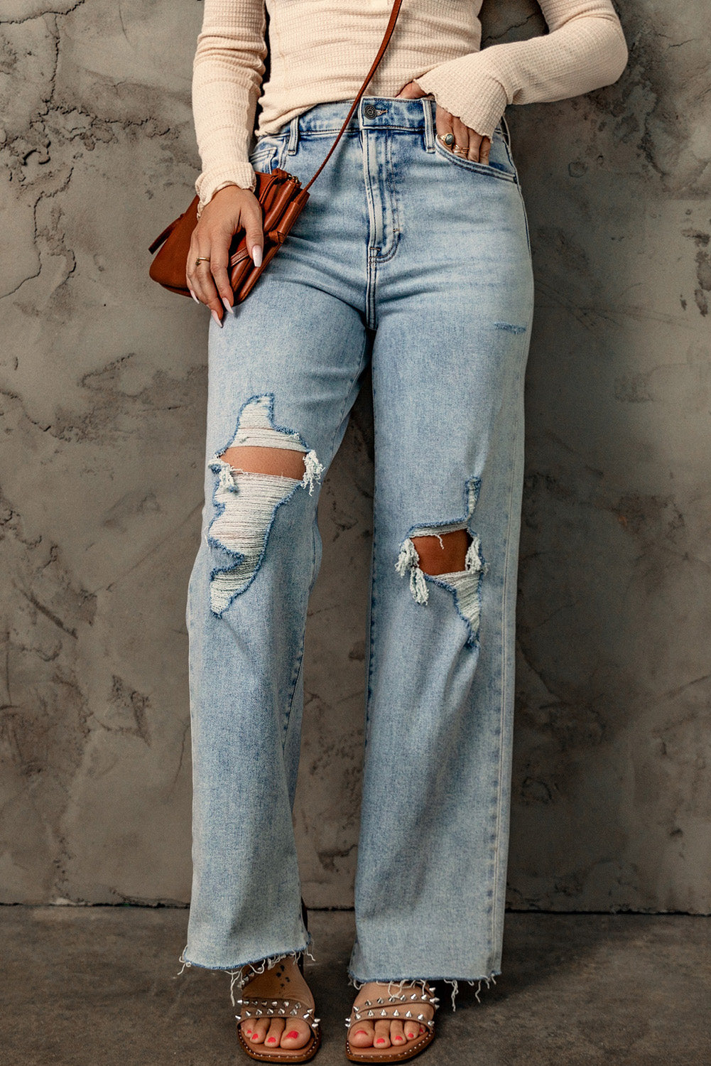 A pair of blue vintage-style jeans with a frayed hem, multiple holes, and a straight, loose-fitting silhouette